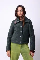 Campera corta de poliéster texturizado color verde oscuro, con cuello camisero, cierre frontal con botones a presión, bolsillos delanteros y forro interior. Incluye pins decorativos.