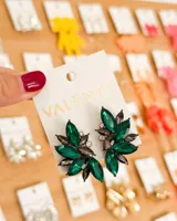 Aretes tipo racimo de cristales facetados, con forma asimétrica. Los cristales son de color verde esmeralda y gris oscuro, con algunos cristales transparentes pequeños. La base es de metal oscuro.