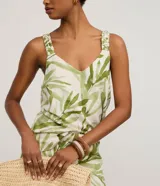 Musculosa femenina confeccionada en una mezcla de viscosa y lino, con estampado de follaje verde sobre fondo crudo. Presenta un cuello en V y breteles anchos con detalle fruncido, ofreciendo un calce regular y fluido.