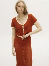 Top tejido calado color azul petróleo con cuello en V y botones carey. Tiene mangas cortas y puños en color amarillo contrastante.