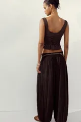 Top marrón con escote redondo y tirantes finos. Tejido fruncido con lazadas frontales y bajo asimétrico con encaje.