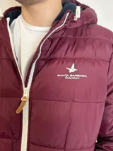 Campera inflada color ocre con capucha, cierre frontal con cremallera y logo de la marca bordado en el pecho.