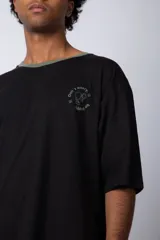 Remera color arena con manga corta negra, cuello redondo con ribete negro y estampado pequeño en el pecho con la frase "Don't worry be happy".