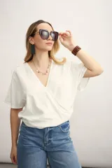 Blusa blanca con escote en V cruzado, mangas cortas y corte holgado.