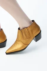 Bota de caña baja en piel color dorado, con cortes verticales y horizontales, tacón bajo y punta alargada.