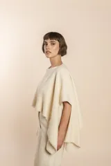 Poncho color beige con diseño a cuadros, cuello bote y terminaciones desflecadas. Tiene aberturas para los brazos en los laterales y detalles en cuero.