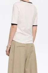 Camiseta blanca de algodón con cuello redondo y mangas cortas con ribete negro. Logotipo de la marca bordado en el pecho.