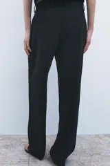 Pantalón negro de tiro medio con trabillas en la cintura, bolsillos delanteros, pierna recta y cierre frontal con cremallera, botón y gancho metálico.