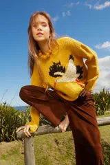 Sweater tejido de lana color amarillo con bordado de cigüeña en el frente y detalle floral en la manga.