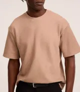 Remera color beige de corte boxy, con escote redondo y mangas cortas. Confeccionada en tejido acanalado de algodón y poliéster.