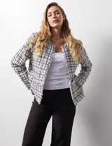 Chaqueta en tejido tweed a cuadrillé blanco y negro, marca Nanette. Cuello a la base y abertura central. Delantera con bolsillos aplicados. Manga larga, puño con botones. Terminación desflecada. Forro interno.