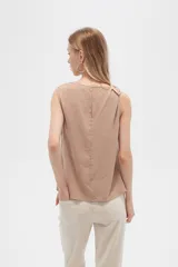Blusa color beige de poliéster, sin mangas, con cuello asimétrico y detalle de drapeado en los hombros.