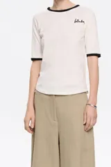 Camiseta blanca de algodón con cuello redondo y mangas cortas con ribete negro. Logotipo de la marca bordado en el pecho.