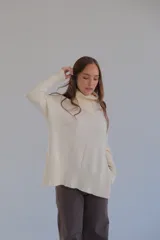 Sweater color crema de corte recto con cuello alto y aberturas laterales.