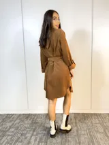 Sobre camisa marrón con cuello camisero, cierre frontal con botones y cinturón con hebilla metálica.