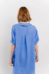 Vestido camisero corto color verde oliva, confeccionado en lino 100%. Tiene botones en la parte delantera, cuello camisero, mangas cortas con botón para arremangar y bolsillos laterales.