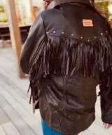 Campera marrón de cuero con cuello camisero, cierre frontal con botones a presión, bolsillos laterales y mangas largas con flecos.