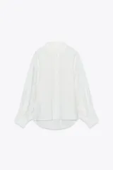 Camisa blanca de lino con cuello clásico, manga larga con puños abotonados y bajo asimétrico.