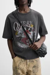 Camiseta negra con cuello redondo y mangas cortas. Estampado frontal con la frase "Cherry Pill Blush Delight" y una ilustración de una mujer en un cohete. Tiene un efecto de lavado que le da una apariencia única.