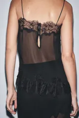 Top negro semitransparente de tejido plisado con escote pico y tirantes finos. Detalle de encaje combinado a tono y cierre en la espalda con botones forrados.