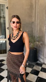 Falda corta tejida a mano en crochet, con diseño a rayas horizontales en tonos marrón oscuro y dorado brillante. Presenta un borde inferior con flecos largos y abundantes.