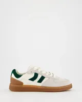 Championes deportivos Coolway modelo Goal, color blanco hueso con detalles en verde oscuro y suela marrón. Confeccionados en serraje y piel, con cordones planos de algodón intercambiables.