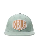Gorra verde agua de pana con parche frontal con las letras KBLG en blanco y contorno marrón.