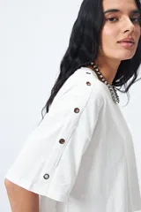Remera blanca cropped de mangas cortas amplias con ojales metálicos a lo largo de las mangas.
