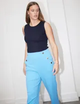 Pantalón largo de crepe elastizado color verde, de corte recto, con bolsillos delanteros y apliques de botones metálicos.