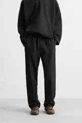 Pantalón wide fit confeccionado en tejido de algodón con interior en rizo, color negro. Cintura elástica ajustable con cordón interior, bolsillos frontales y detalle de bolsillo trasero de vivo. Perneras con costura frontal y efecto lavado.