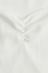Top corto blanco de punto acanalado fino de algodón, con mangas japonesas, costura fruncida en el busto, escote corazón con ribete de picot y bajo recto.
