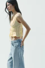 Top amarillo con estampado de cuadros vichy blancos, escote en pico, sin mangas, con detalle de elásticos en la cintura y cierre frontal con lazadas.