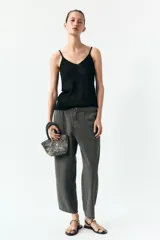 Pantalón gris oscuro de tiro alto con cintura elástica, bolsillos delanteros y falsos bolsillos con solapa en la espalda. Cierre frontal con cremallera y botón.