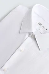Camisa blanca de manga larga, corte slim fit, con cuello italiano y cierre frontal de botonadura. Presenta un patrón de rayas verticales muy finas y sutiles.