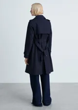 Trench coat azul marino con doble botonadura, cinturón ajustable, cuello de solapa, trabillas en los puños y abertura posterior en el bajo.
