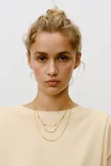 Set de tres collares dorados de diferentes largos. Uno es de eslabones metálicos con piezas circulares, otro es de cordón metálico con abalorios y perlas naturales, y el tercero es de cordón metálico liso.
