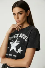 Remera corta de algodón con efecto lavado (acid wash) en color negro. Presenta un estampado frontal en blanco con texto "ROCK SOUL SINCE 2006 ON TOUR ROCK" y estrellas.