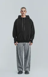 Hoodie negro oversize de frisa premium con capucha ajustable, cordones con texto y puños elastizados.