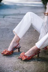 Zapato de tacón destalonado con estampado animal print en tonos naranja y marrón, con lazo doble en la parte delantera y tira trasera con hebilla. Tacón cuadrado de 2,5 cm y suela de cuero.