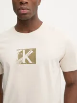 Remera color crema de algodón regenerado, con cuello redondo y logotipo de Calvin Klein en un recuadro color ocre.