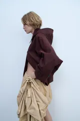 Trench corto color negro, con cuello solapa y capucha desmontable mediante botones. Manga larga tipo murciélago acabada en trabilla ajustable. Bolsillos laterales. Forro interior combinado. Cierre frontal con botones. Tejido repelente al agua.