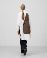 Camisa oversize blanca de manga larga con cuello solapa y botonadura frontal. Presenta una pieza superpuesta en la espalda que corresponde al delantero de un blazer.