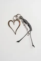 Llavero plateado con dije metálico en forma de corazón y cordón negro. Incluye cadena de eslabones plateados y tiras de cuero trenzado.