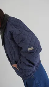 Campera puffer azul marino con diseño acolchado de rombos, cuello de cuero sintético negro, mangas largas abullonadas con puños elásticos y cierre frontal con cremallera.