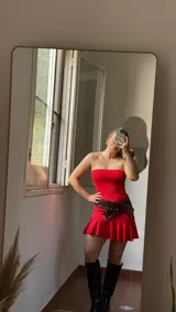 Vestido corto rojo sin mangas, confeccionado en jersey de lycra con delantera doble y corte ajustado. Incluye cinturón marrón con tachas.