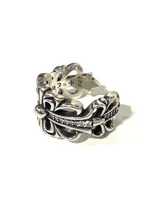 Anillo plateado con diseño de flor de lis y pequeños cristales incrustados.