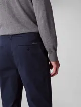 Pantalón chino de corte slim color azul marino, confeccionado en algodón y elastano. Presenta cierre con cremallera y botón, diseño clásico de cuatro bolsillos y logo de Calvin Klein bordado en la parte posterior.
