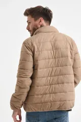 Campera acolchada color beige, con cuello alto y cierre frontal. Presenta costuras horizontales que crean el efecto capitoné.