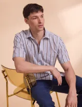 Camisa de manga corta con rayas verticales en tonos celeste, blanco, tostado y negro. Tiene cuello clásico, cierre con botones y bolsillo en el pecho.