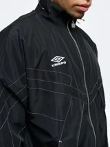 Campera deportiva Umbro de nylon con diseño color block en blanco, azul y rojo. Tiene cuello alto, cierre frontal con cremallera y bolsillos laterales. Logo de Umbro bordado en el pecho.